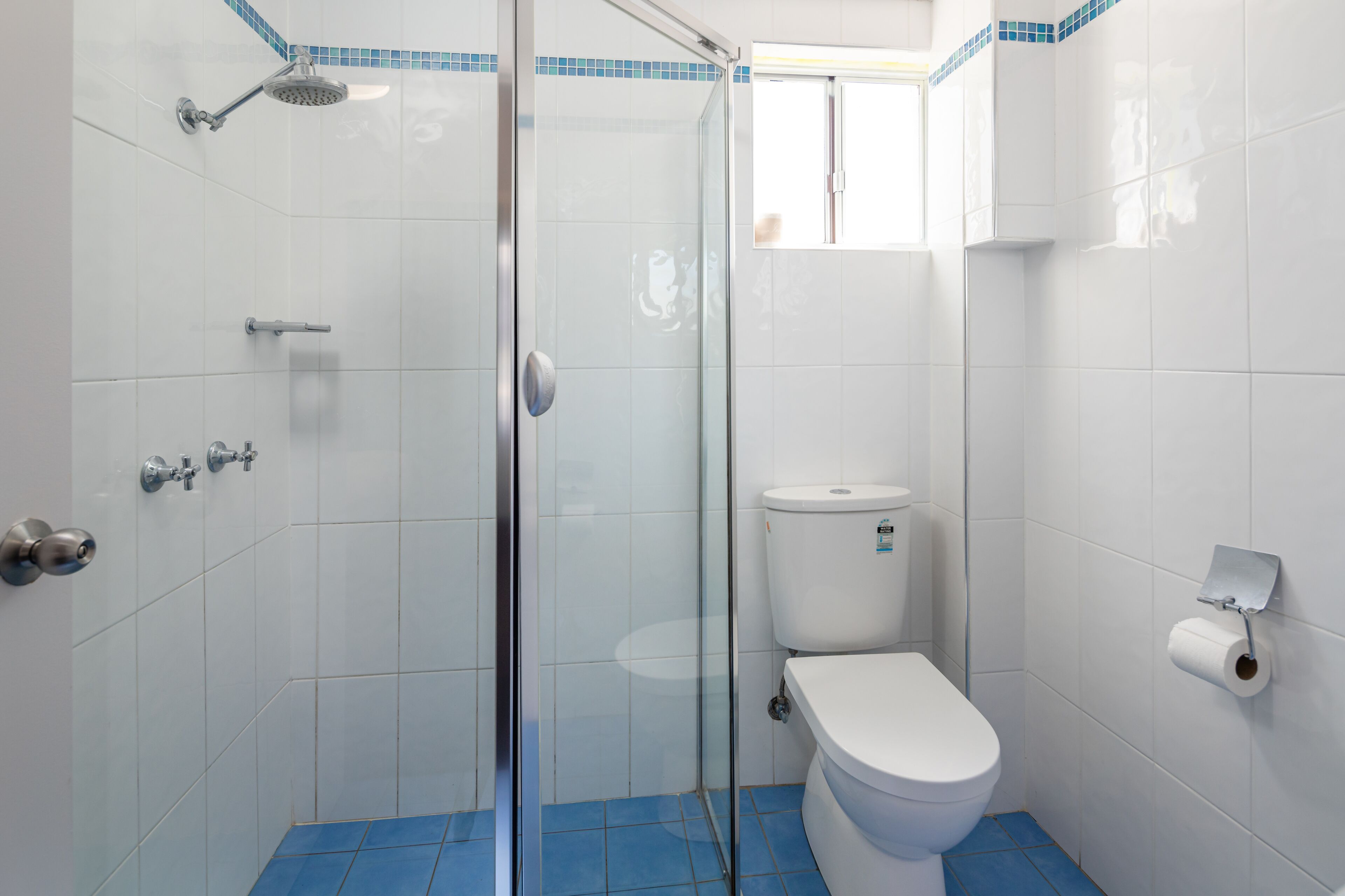 Ein Badezimmer mit Duschkabine aus Glas, Toilette und blau gefliestem Boden.
