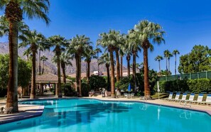 Une piscine entourée de palmiers, avec une chaîne de montagnes en arrière-plan.