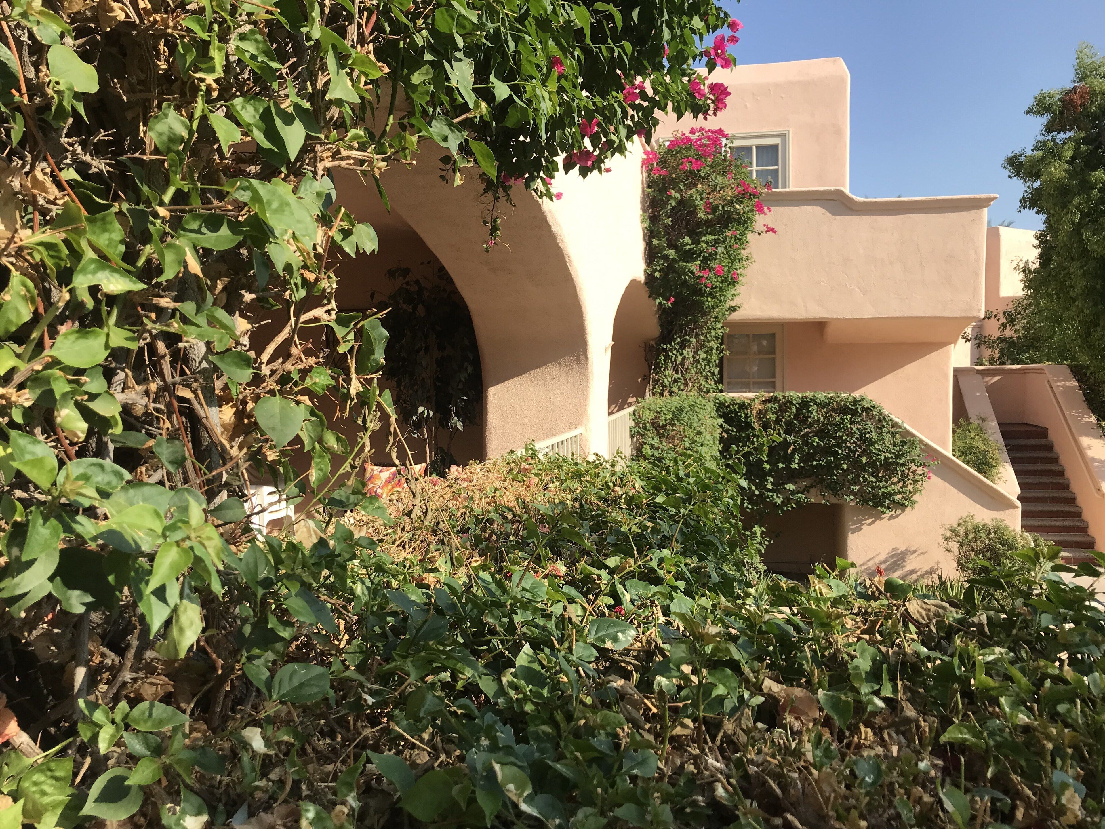 Un edificio de fachada color beige, una escalera y follaje a su alrededor.