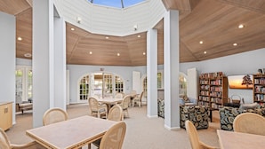 A spacious interior with a high ceiling, open-plan layout, and a central dining area with wicker furniture. - Three Pools. Mountain Views. Just Blocks from vibrant downtown nightlife! (Palm Springs)