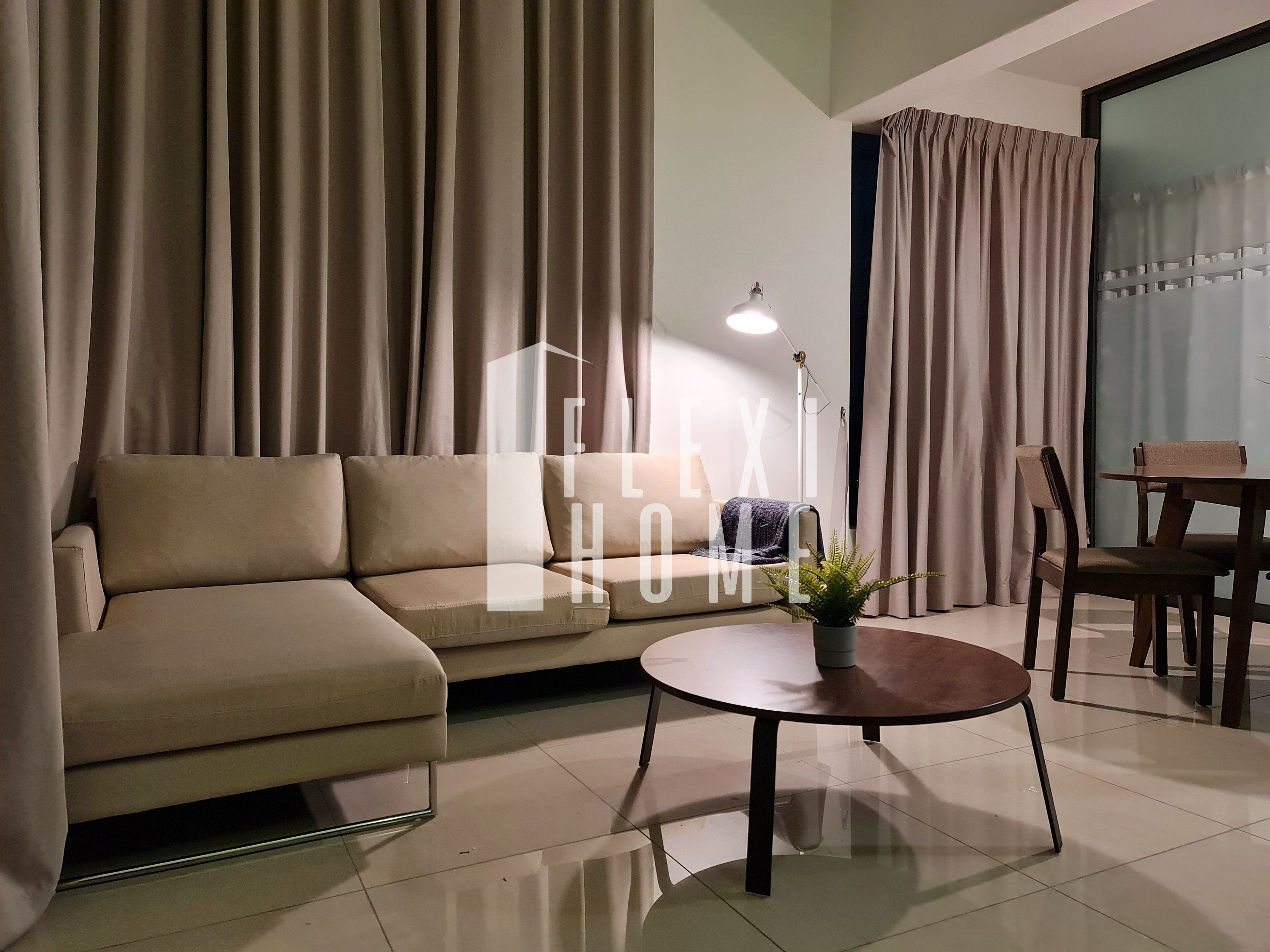 Uma sala de estar moderna com um sofá, uma mesa de centro redonda com uma planta, uma mesa de jantar com cadeiras e uma janela grande com cortinas.