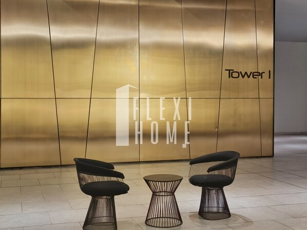 Un interior moderno con una pared grande que muestra 'Flexi Home' y 'Tower I'. Hay dos sillas negras y una mesita en primer plano.