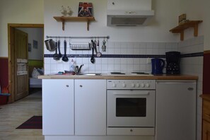 A compact kitchen with a built-in oven, a coffee maker, and hanging utensils.