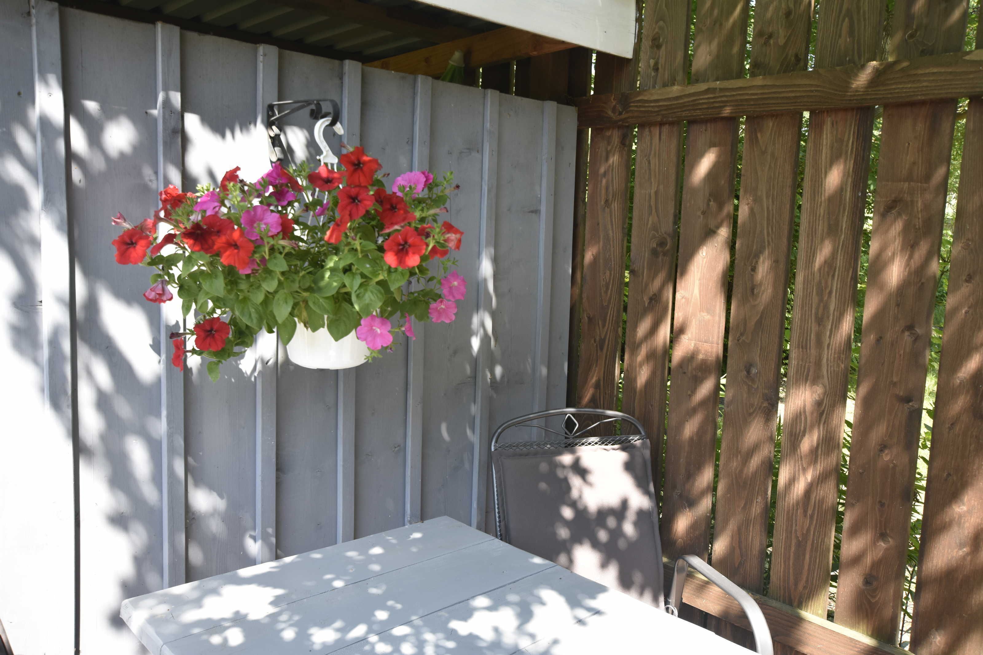 Une table et une chaise blanches sont placées sous un pot de fleurs suspendu, orné de fleurs rouges et roses.