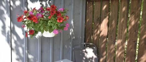 Un juego de mesa y sillas blancos bajo una maceta colgante con flores rojas y rosas.