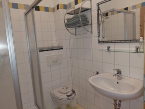 A bathroom with a shower, toilet, sink, and a towel rack.