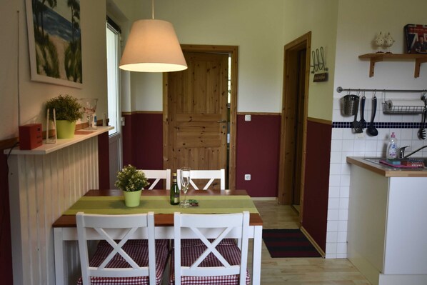 A dining area with a table, chairs, a hanging lamp, a wooden door, and kitchen utensils on the wall.