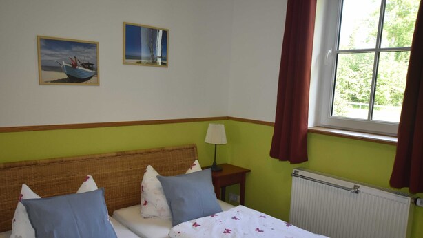 Una habitación con dos camas, un ventanal con cortinas, un radiador y dos cuadros colgados en la pared.