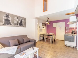 Een moderne woonkamer met een grijze bank, een salontafel met een tijdschrift, en een eethoek met een tafel en stoelen.