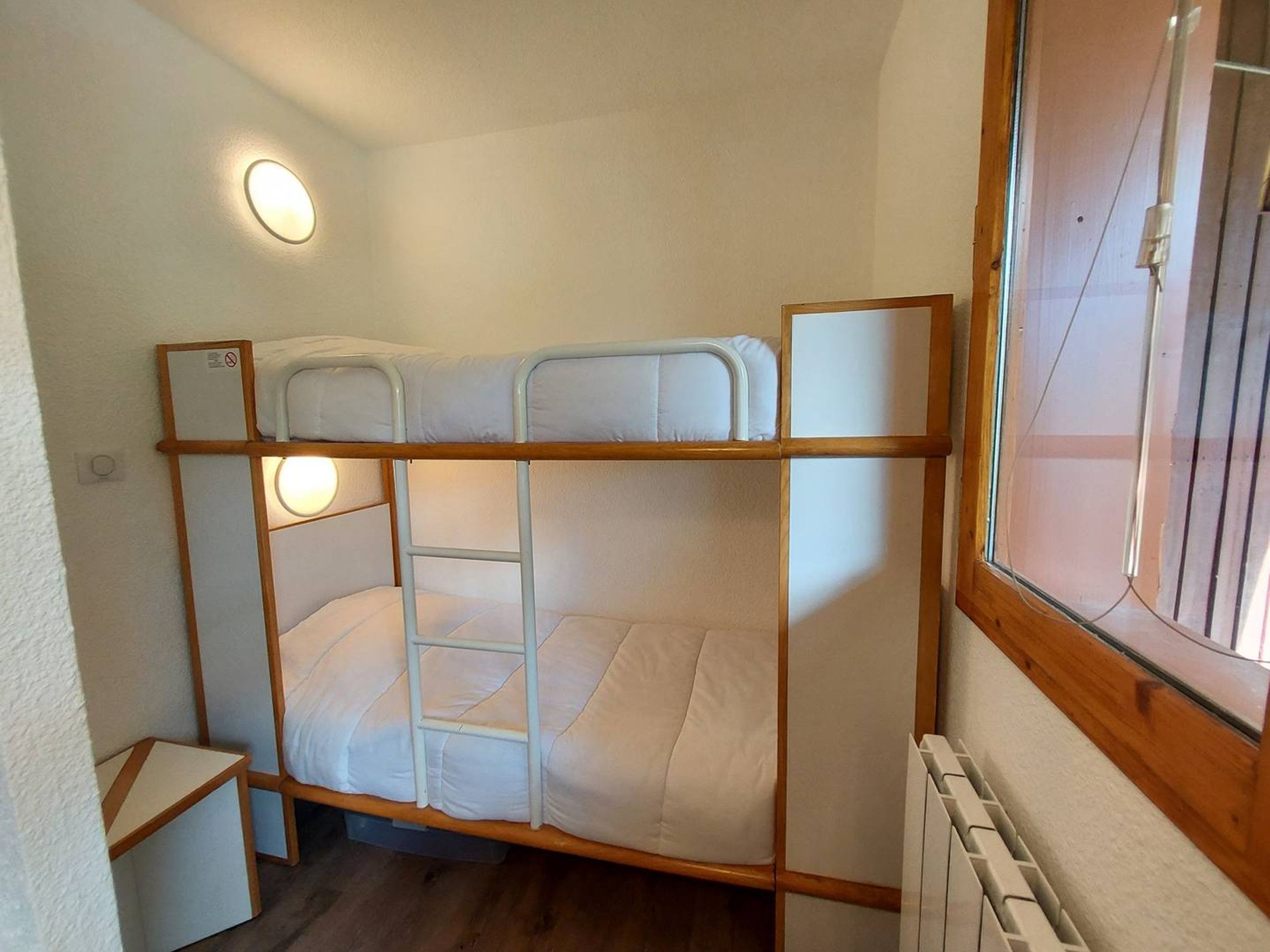 Ein Schlafraum mit Etagenbetten, einer kleinen Tisch und einem Fenster mit Jalousien.