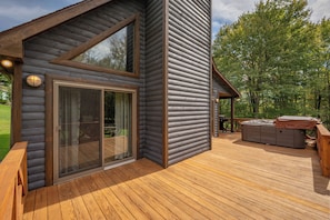 A log cabin with a deck, large sliding glass doors, and a hot tub.