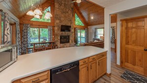 A spacious kitchen with a stone fireplace, wooden cabinets, and a large island. - Dog Friendly Cozy Escape w/ Hot Tub & Porch Views (Swanton)