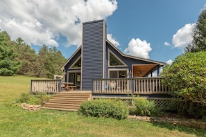 A modern house with a prominent central tower, a wooden deck, and a well-maintained lawn.