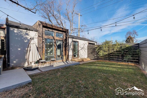A modern house with a large glass window, a patio with outdoor furniture, and a well-maintained lawn. - Sunny Carriage House in Denver • Patio + Firepit (Denver)