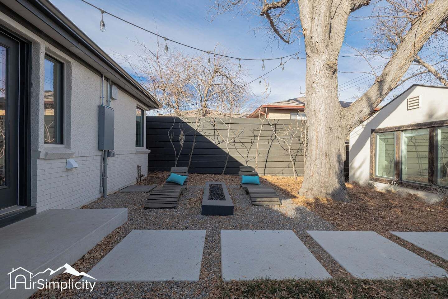 A modern backyard with a patio area, a tree, and a house with a white exterior.