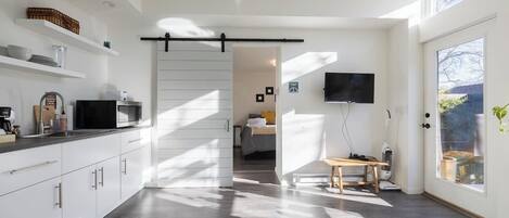 A modern kitchen with white cabinetry, a black countertop, and a sliding door leading to a bedroom.