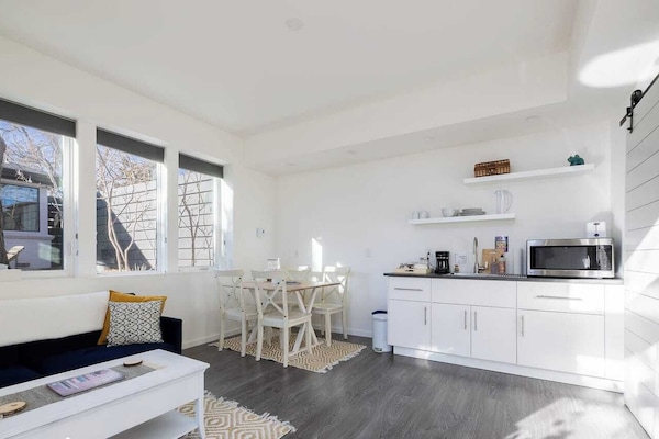 - Sleek white kitchenette stocked with essentials for morning coffee or light bites
- Open shelving and minimal decor keep the space fresh, functional, and inviting
- Dining area with seating for four is ideal for meals, games, or remote work session