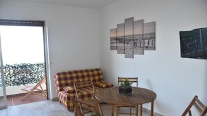 A balcony with a checkered sofa, a wooden table with chairs, and a TV mounted on the wall. - BRILOC Apartment (48 m² - 48 sq ft - ) (Ajaccio)
