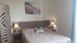 A neatly arranged bedroom with a large bed, two bedside lamps, a decorative wall piece, and a patterned curtain. - BRILOC Apartment (48 m² - 48 sq ft - ) (Ajaccio)