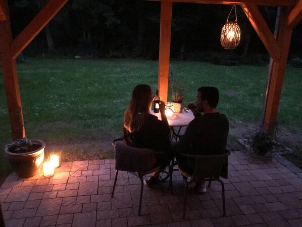 A covered outdoor dining area with a table and chairs, a hanging light fixture, and a potted plant. - Former Forest Ranger's Cabin in Lindewitt (Lindewitt)