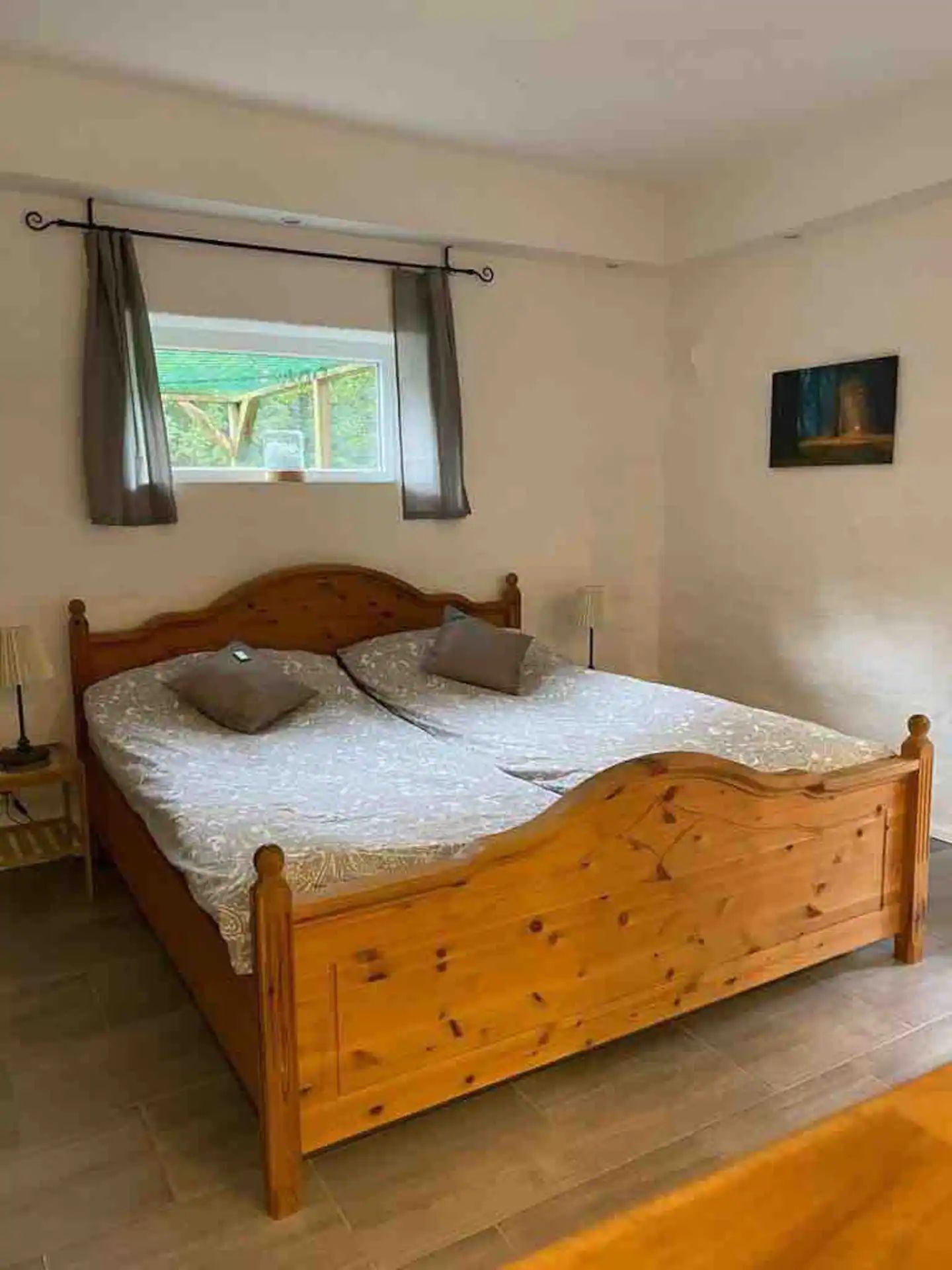 A wooden bed with a headboard, a nightstand, and a window with curtains.