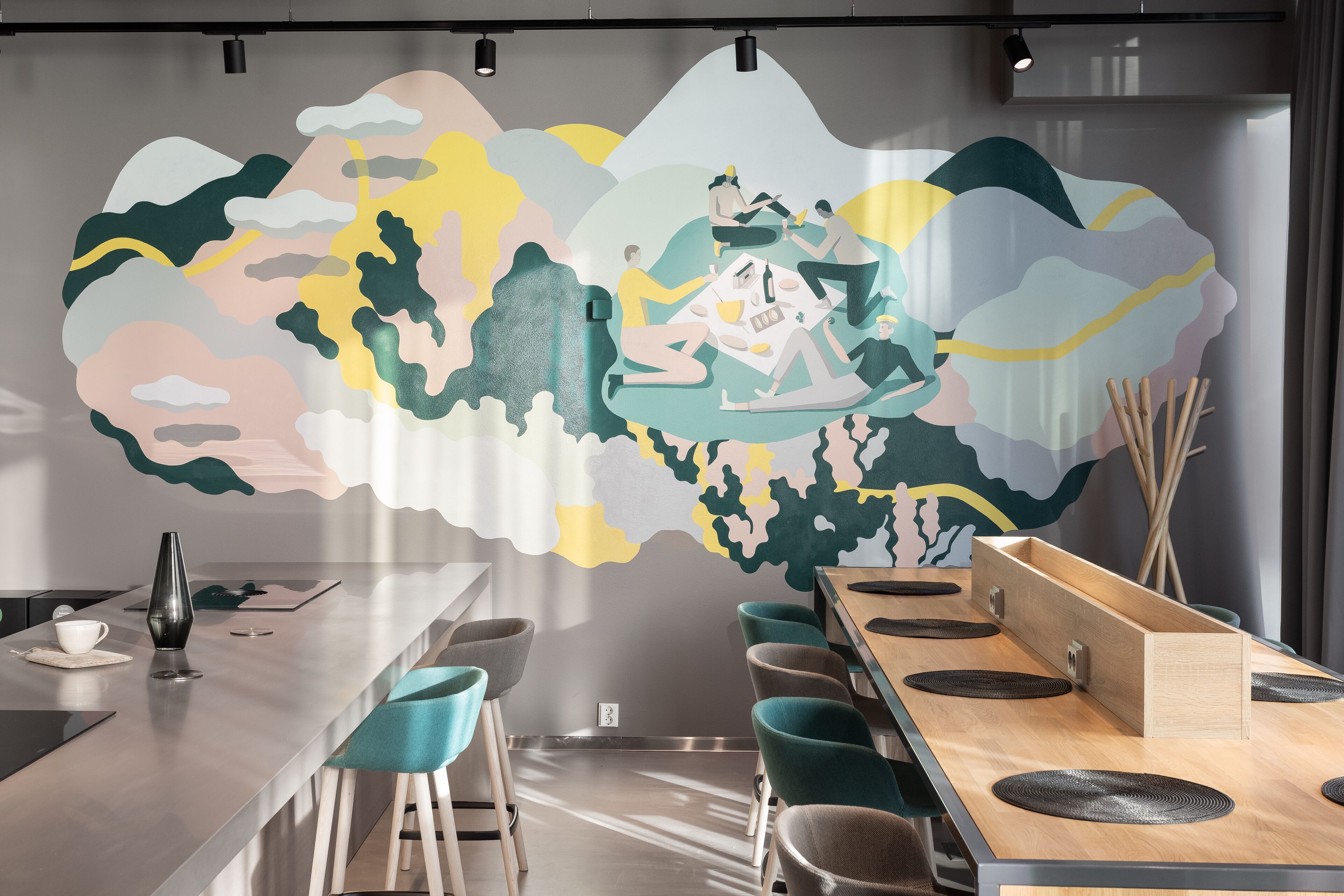 A modern dining area with a long table, teal chairs, and a mural on the wall.