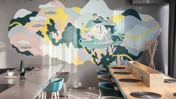 A modern dining area with a long table, teal chairs, and a mural on the wall.