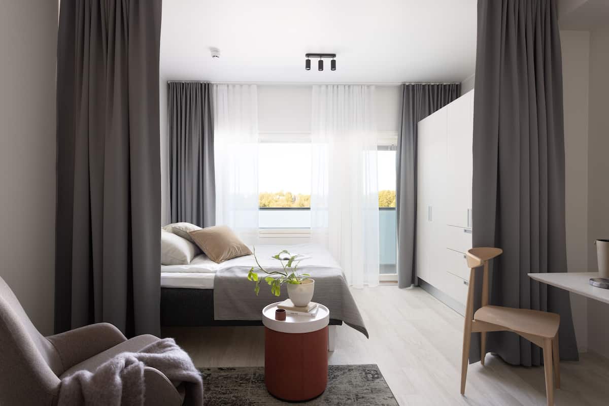 Ein modernes Schlafzimmer mit Bett, Nachttisch, Sessel und Blick auf einen Balkon.