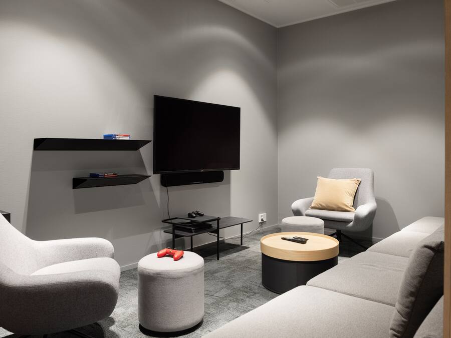 Una sala de estar moderna con televisor de pantalla plana, sofás grises, una mesa de centro y una silla gamer.