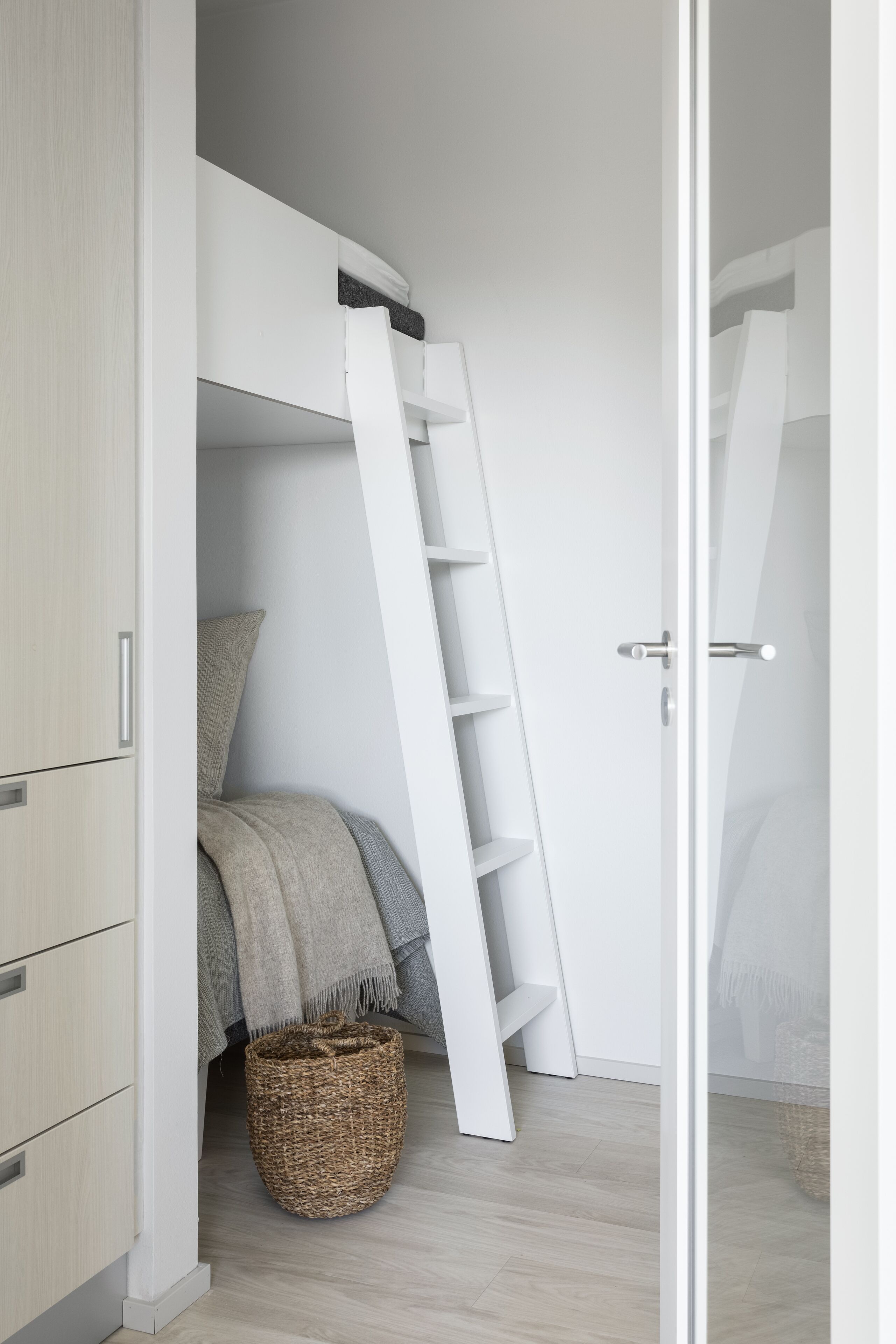 A bedroom with a built-in wardrobe, a ladder, a bed with a grey blanket, and a wicker basket on the floor.