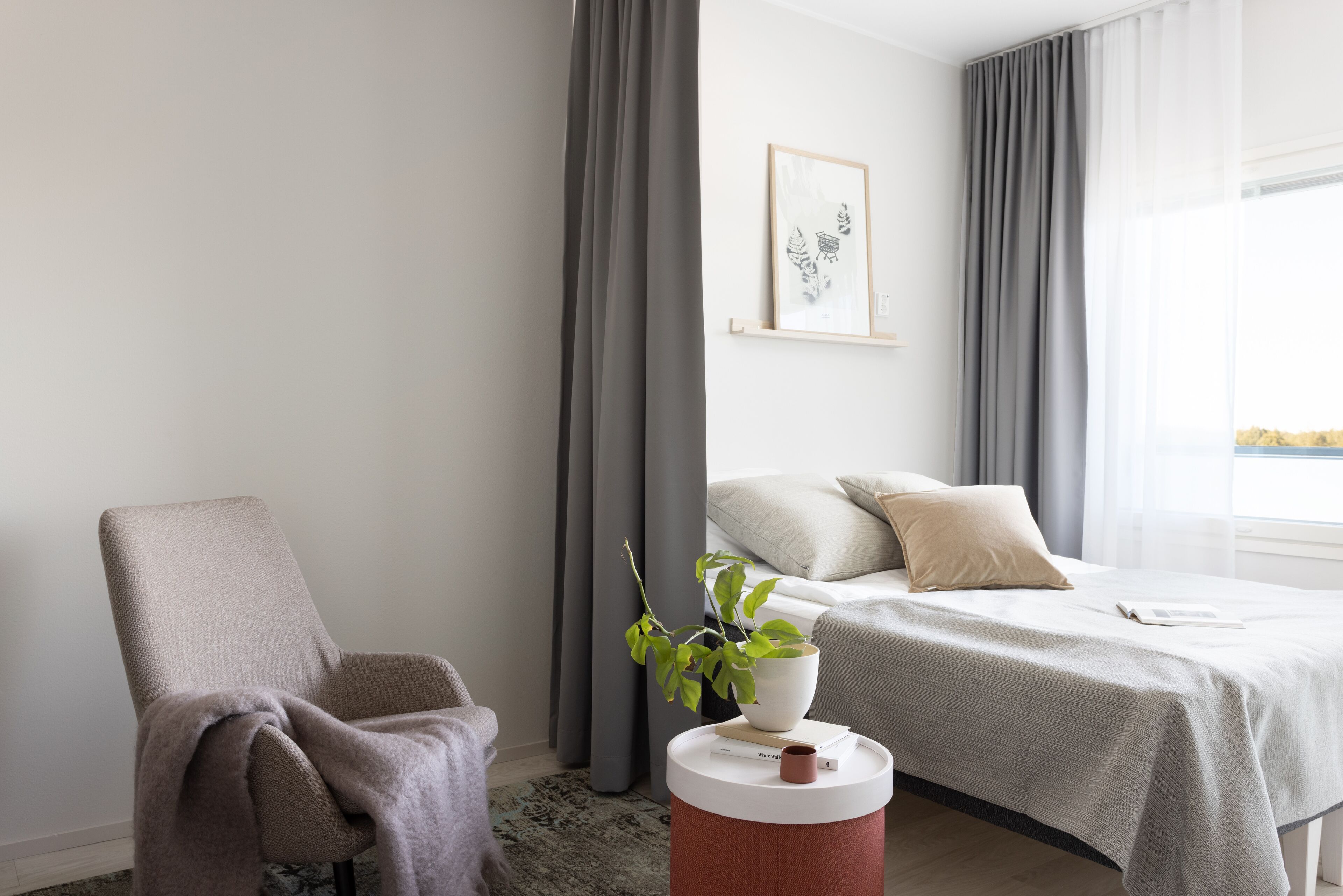 Una habitación de hotel moderna con una cama, una silla, una planta en maceta y una obra de arte enmarcada en la pared.