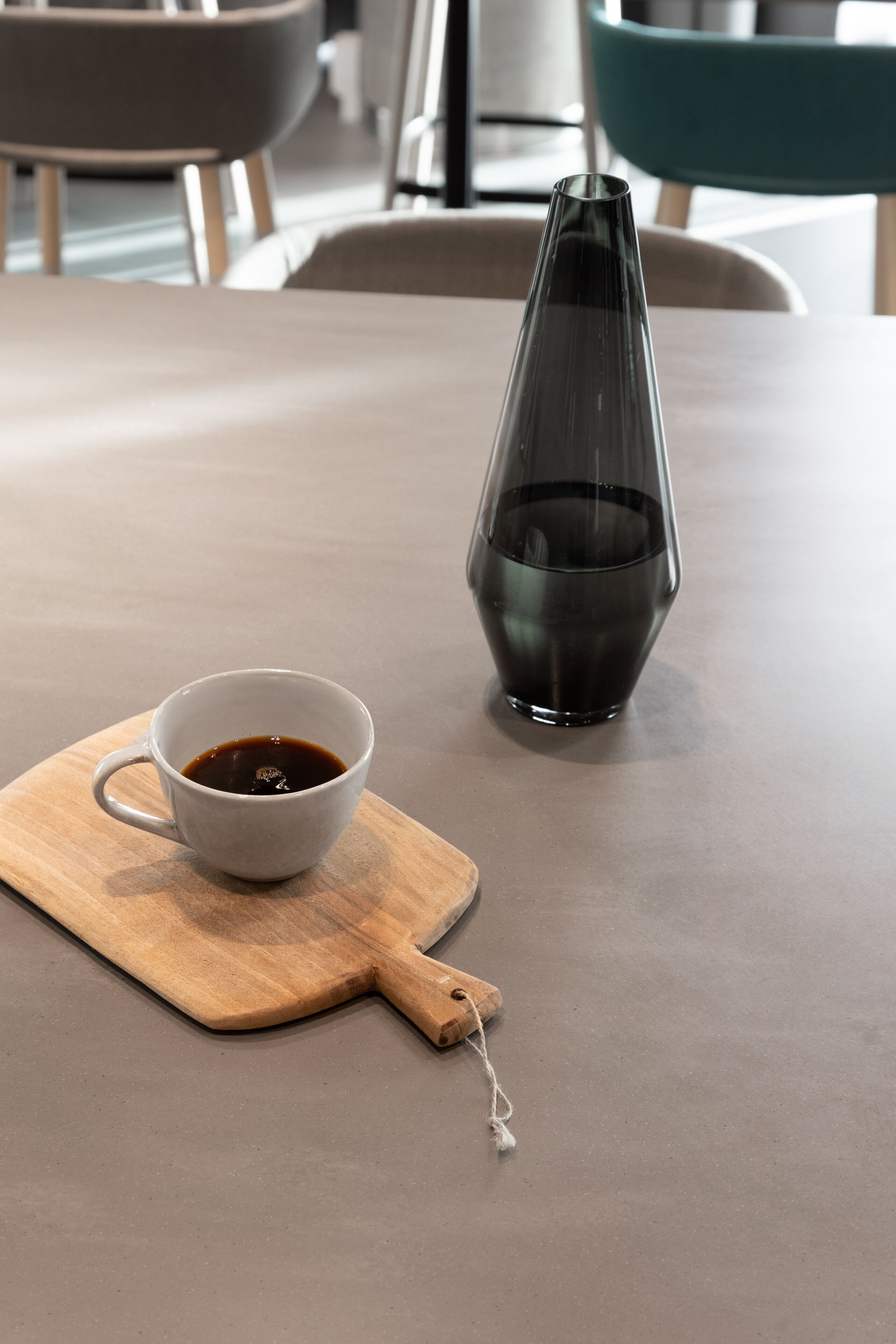 A table with a cup of coffee and a dark glass vase.