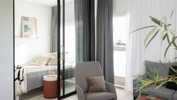 Een moderne hotelkamer met een bed, een grijze fauteuil, een bank en een groot raam met gordijnen.