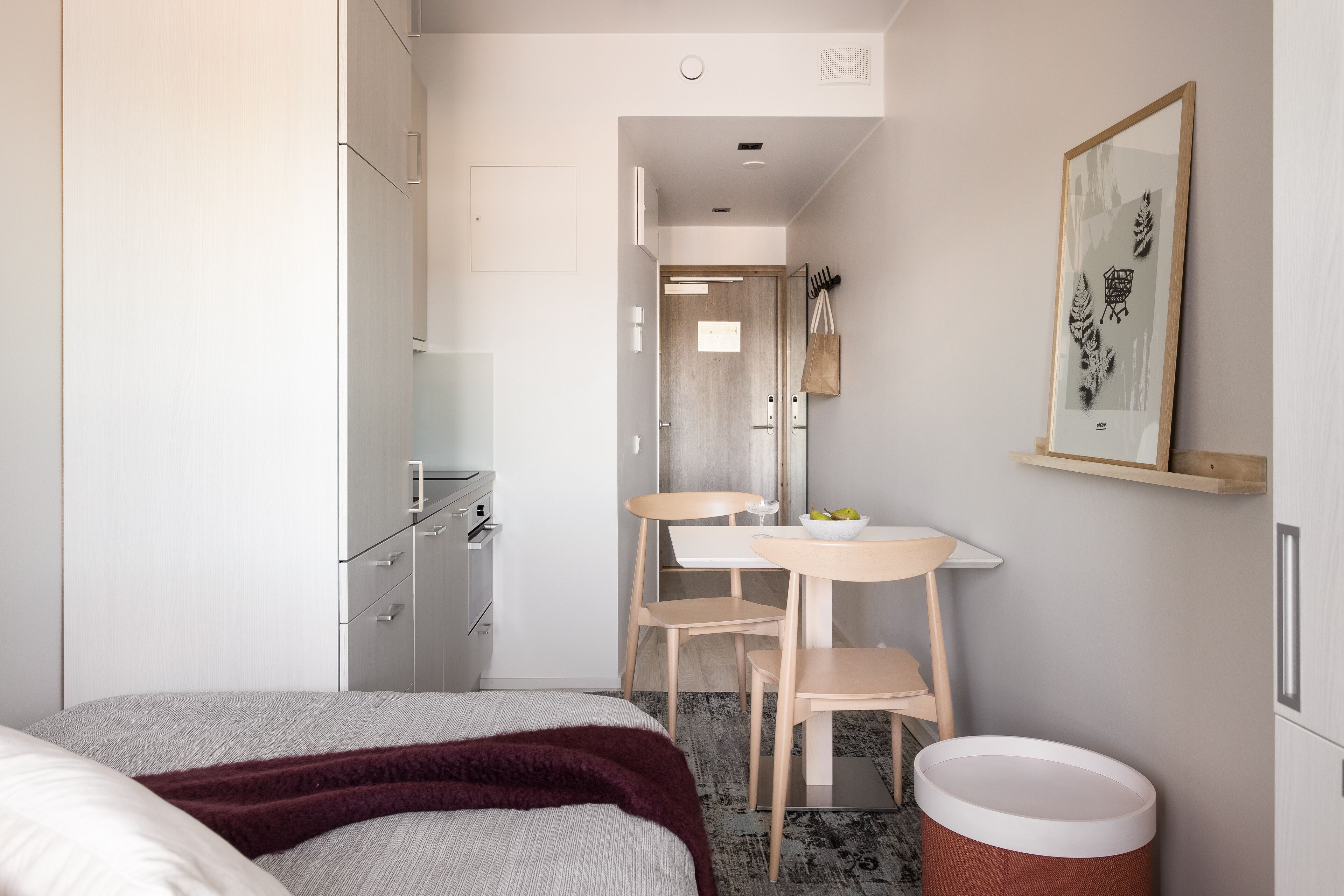 Una habitación de hotel moderna con una cama, una mesita con sillas, un espejo y un cesto de basura.