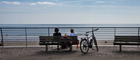 Two people sitting on a bench by a waterfront, with a bicycle parked nearby.