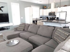 A modern living room with a sectional sofa, a dining table, and a kitchen area in the background.