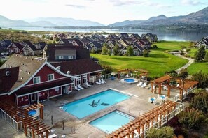 A residential area with a swimming pool, lounge chairs, and a view of a lake and mountains.