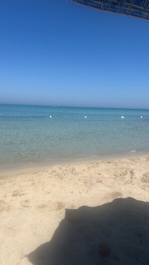 Ein Strand mit klarem Wasser, sandigem Ufer und ein paar Bojen in der Ferne.