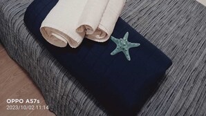 Un llit ben arropat amb un llençol blavastre i gris, dues tovelloles enrere i una decoració de estrella de mar.