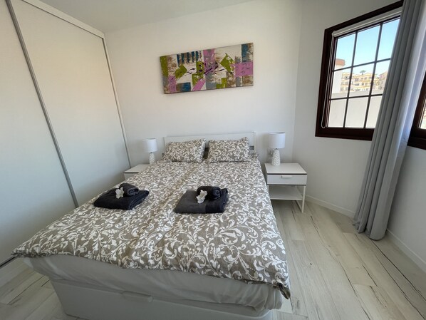 A neatly arranged bedroom with a bed, two bedside tables, a wall-mounted painting, and a window with curtains. - Modern 2 bed apartment (70qm2)  with  oceanview (Costa Adeje)