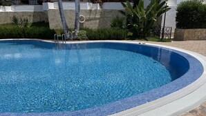Une piscine aux eaux claires et bleues, bordée de carreaux, entourée d’un mur de pierre et d’une végétation luxuriante.