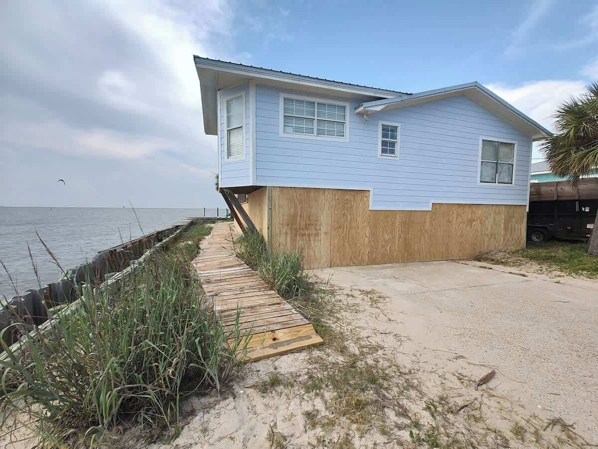 Une maison située sur la côte, dotée d’une terrasse en bois qui mène à une plage de sable.