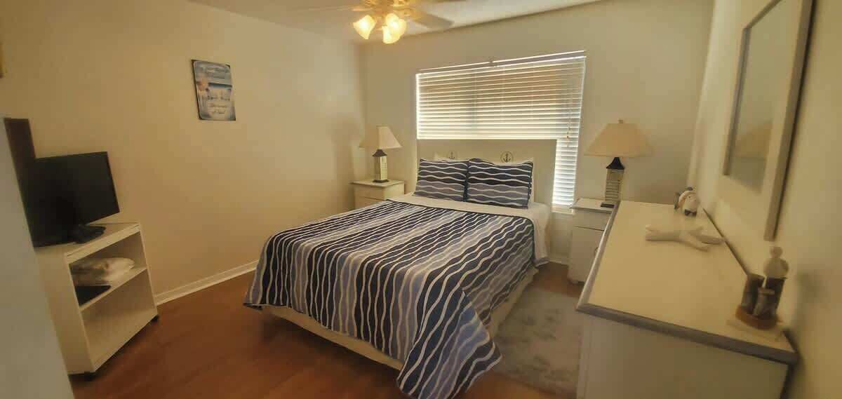 A bedroom with a bed, nightstands, a television, and a desk with a lamp.