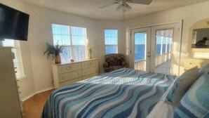 Un dormitorio con cama, cómoda, silla y vista al océano a través de una puerta.