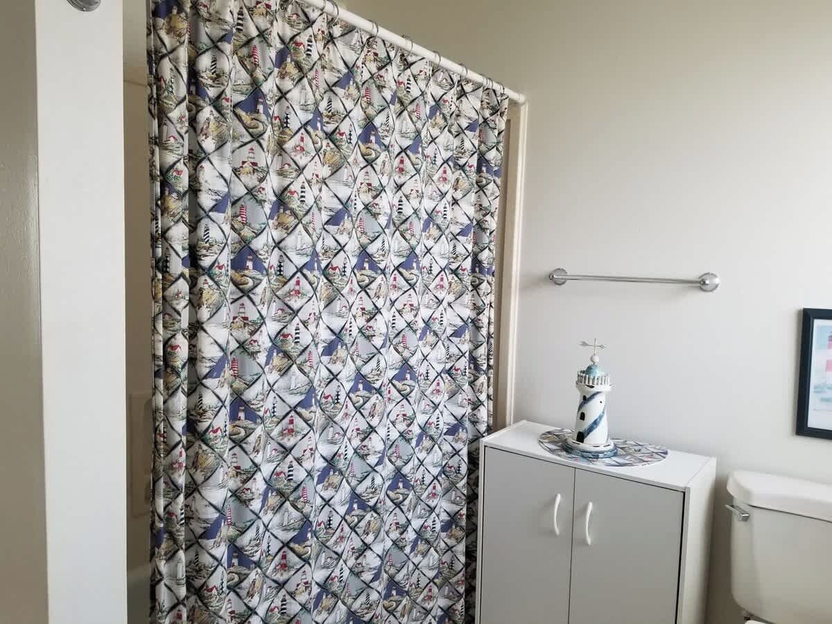 A bathroom with a patterned shower curtain, a small cabinet, and a framed picture on the wall.