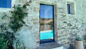 A stone building with a pool, steps leading to the entrance, and potted plants.