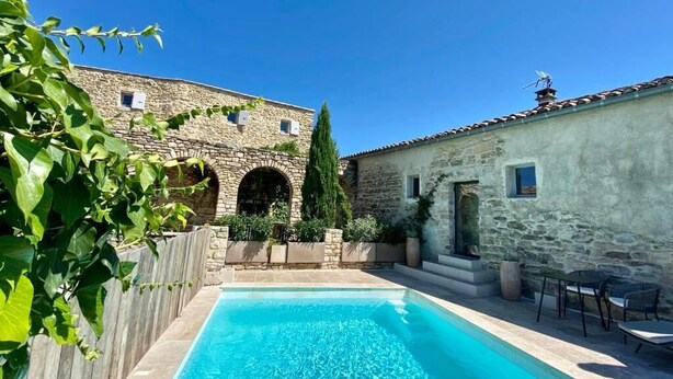A stone building with a swimming pool, outdoor seating, and greenery.