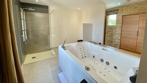 A modern bathroom with a walk-in shower, a large bathtub with multiple jets, and a wooden wardrobe.