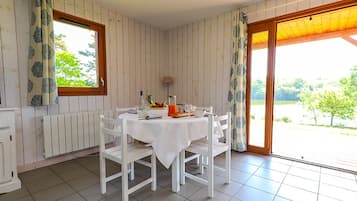 Zona de menjador amb taula preparada per a quatre, cadires blanques, un radiador, finestra amb cortines i vistes a vegetació a l'exterior.
