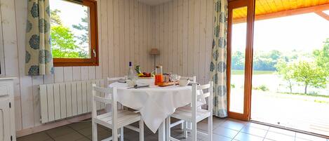 Comedor con una mesa dispuesta para cuatro, sillas blancas, un radiador, una ventana con cortinas y vistas al exterior.